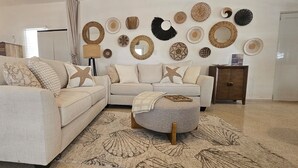 Ett vardagsrum med en beige soffa, en pall och en mönstrad matta.