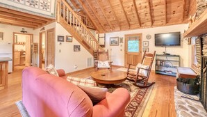Un salon chaleureux avec un plafond en bois, un escalier, une télévision et une cheminée en pierre.