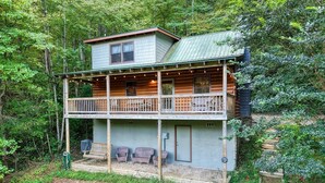 Une cabane en rondins à deux étages, dotée d’un balcon et entourée d’une forêt dense.