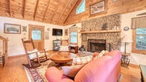 Un intérieur de chalet chaleureux avec une cheminée en pierre, un plafond en bois et un coin salon confortable.
