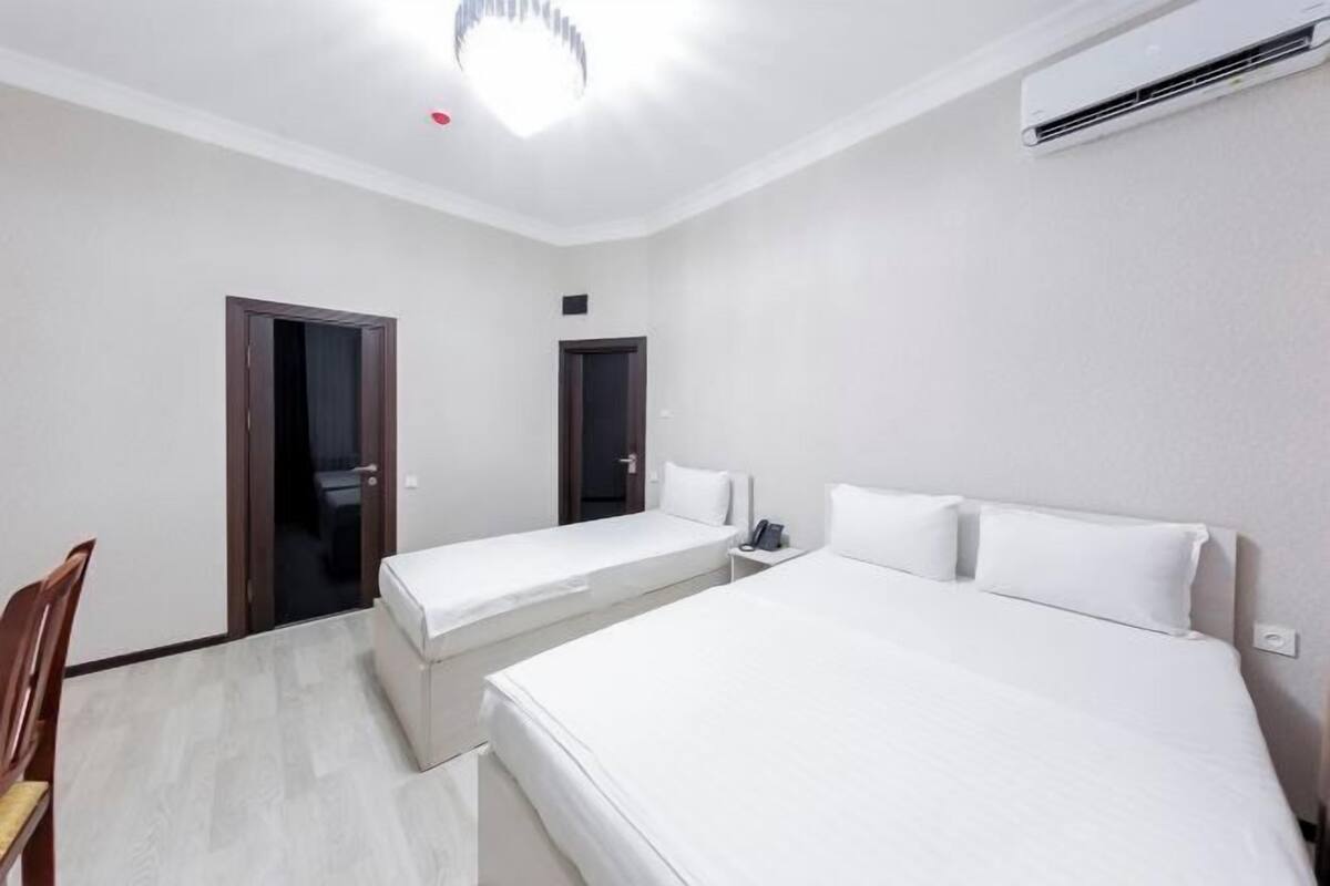 A hotel room with two single beds, a desk with a phone, and an air conditioning unit.
