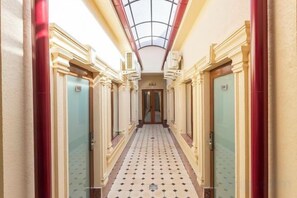 Un pasillo de hotel con puertas a ambos lados, piso estampado y tragaluces arriba.