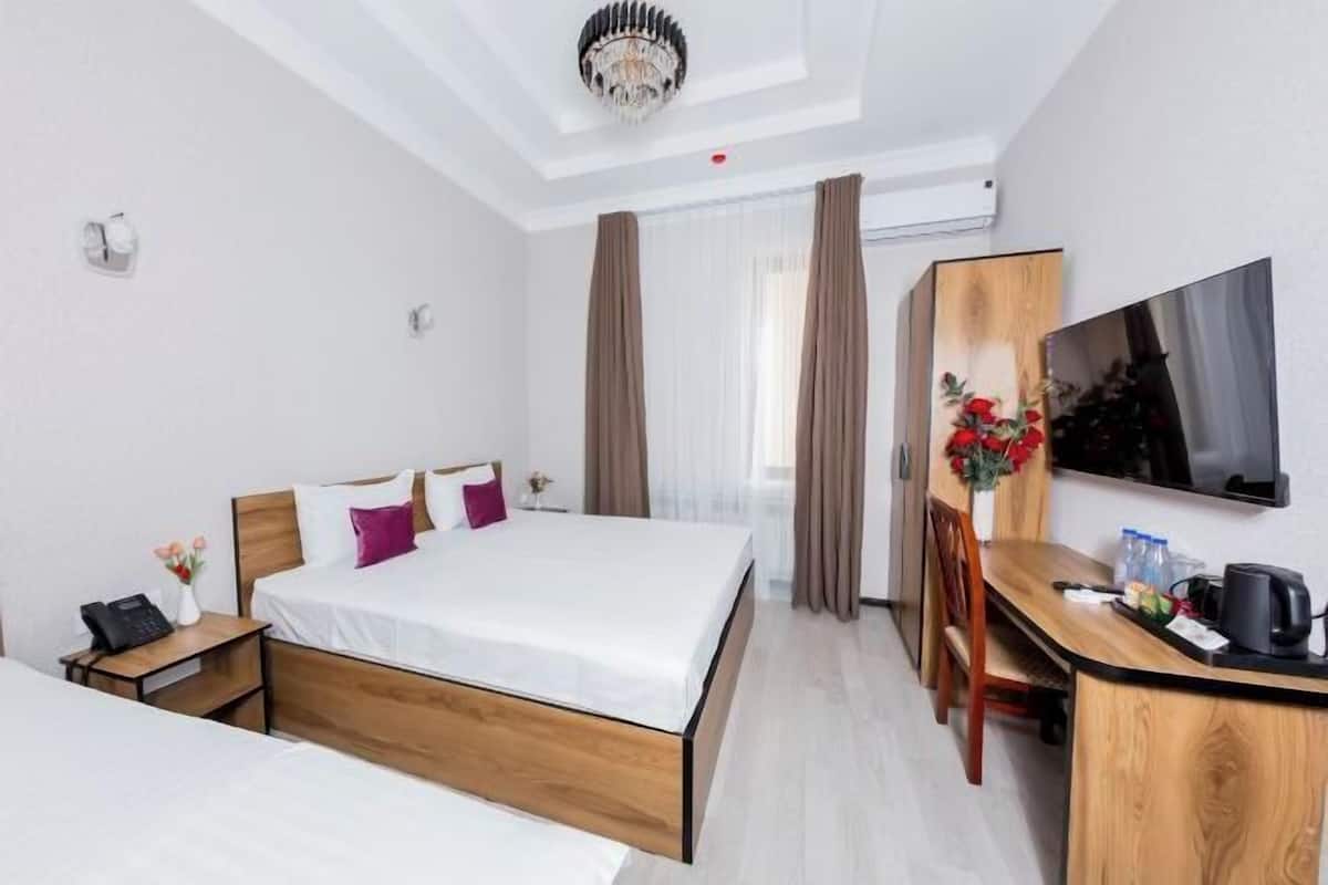 A hotel room with a bed, bedside table, desk, chair, TV, and curtains.