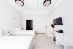 A hotel room with two beds, a desk with a flat-screen TV, and a small seating area.