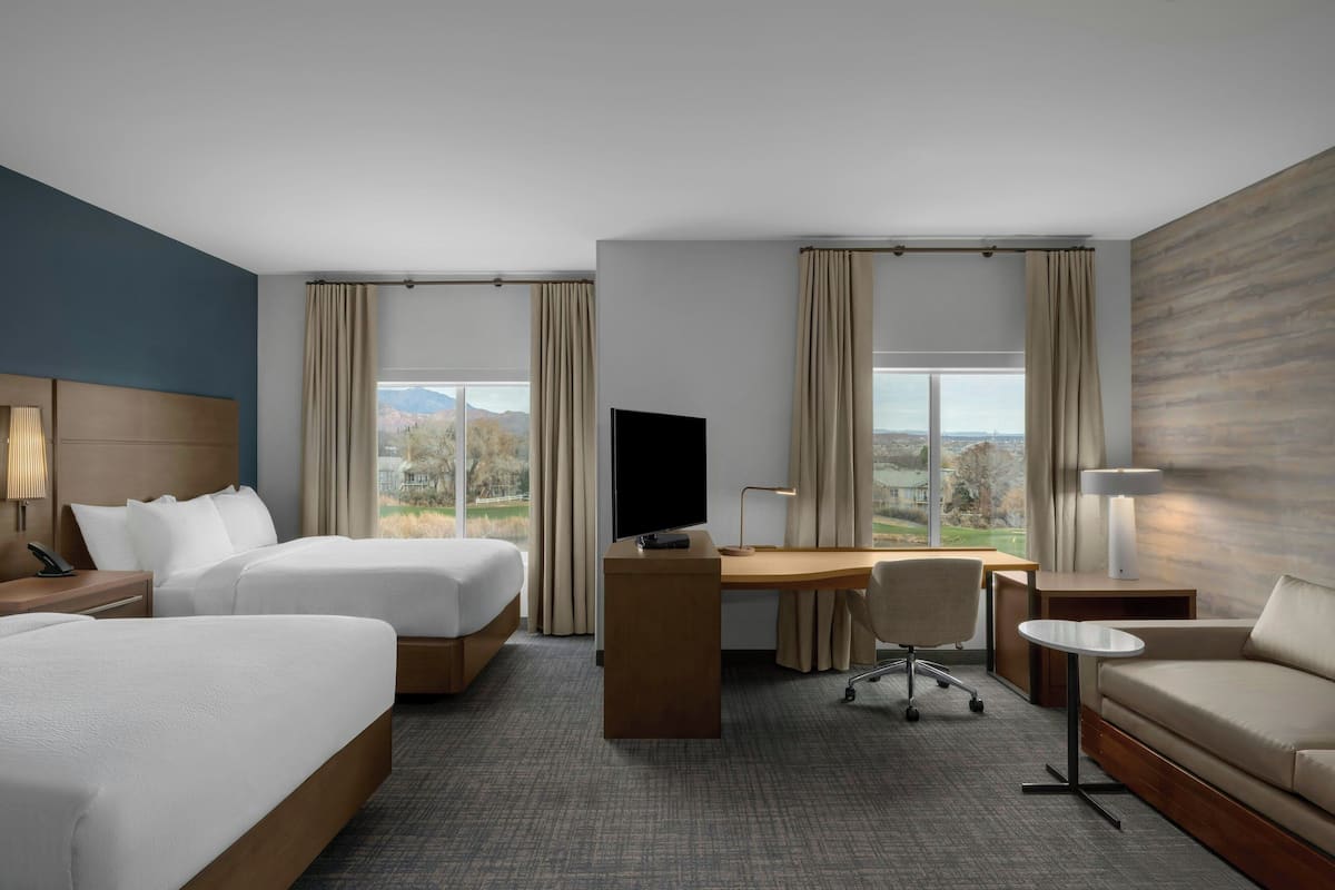 Habitación de hotel con dos camas, un escritorio, televisor, sofá y vistas al exterior.