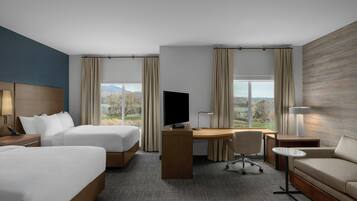 Habitación de hotel con dos camas, un escritorio, televisor, sofá y vistas al exterior.