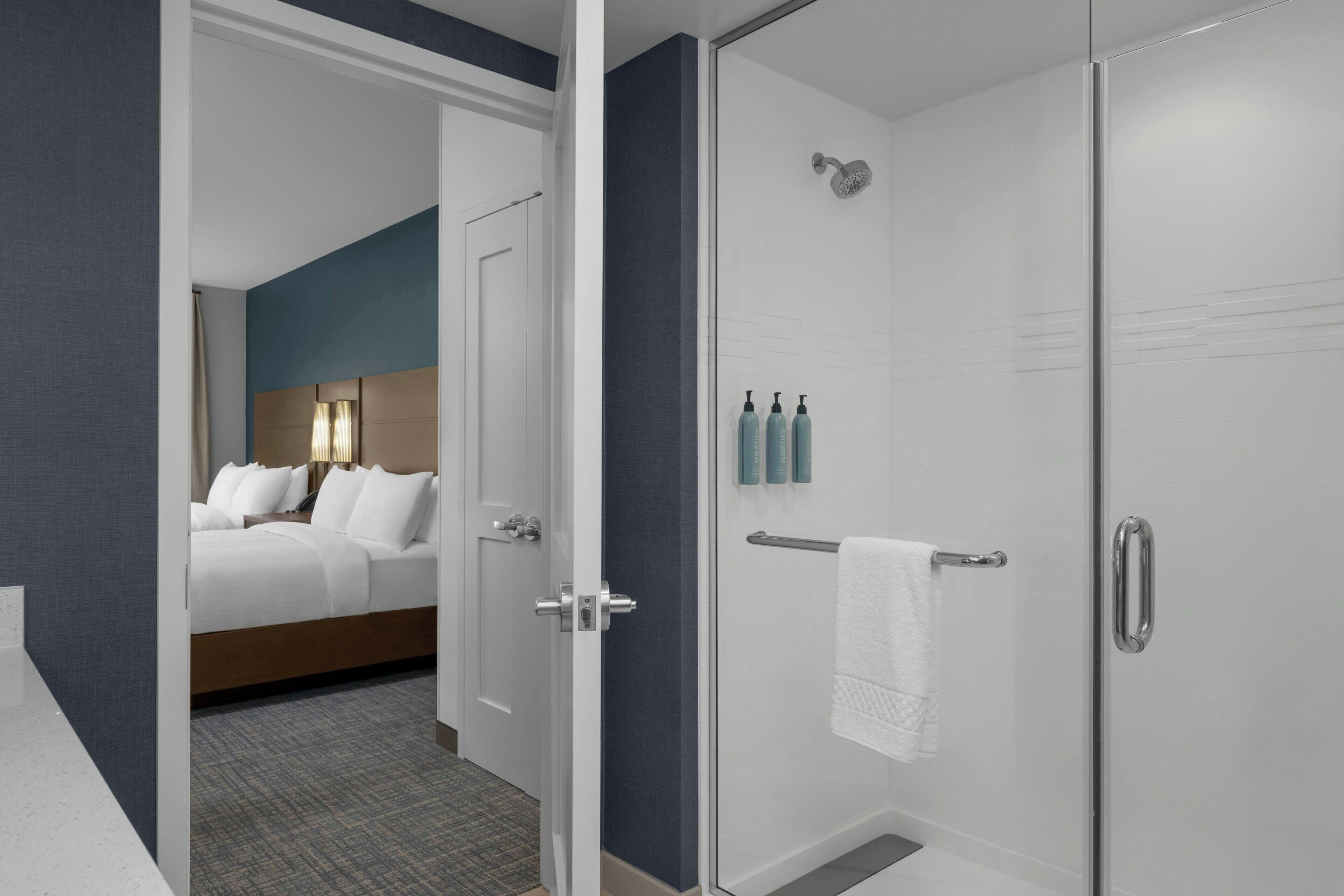 A hotel room with a bed, a shower, and a bathroom with toiletries.