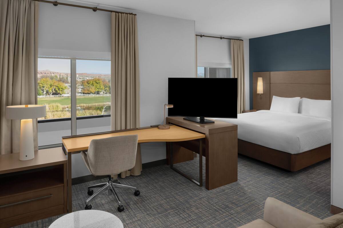 Habitación de hotel con cama, escritorio, silla, televisor y vistas al exterior.