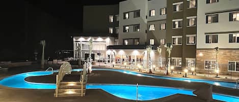 A hotel with a swimming pool, outdoor seating, and a well-lit entrance.
