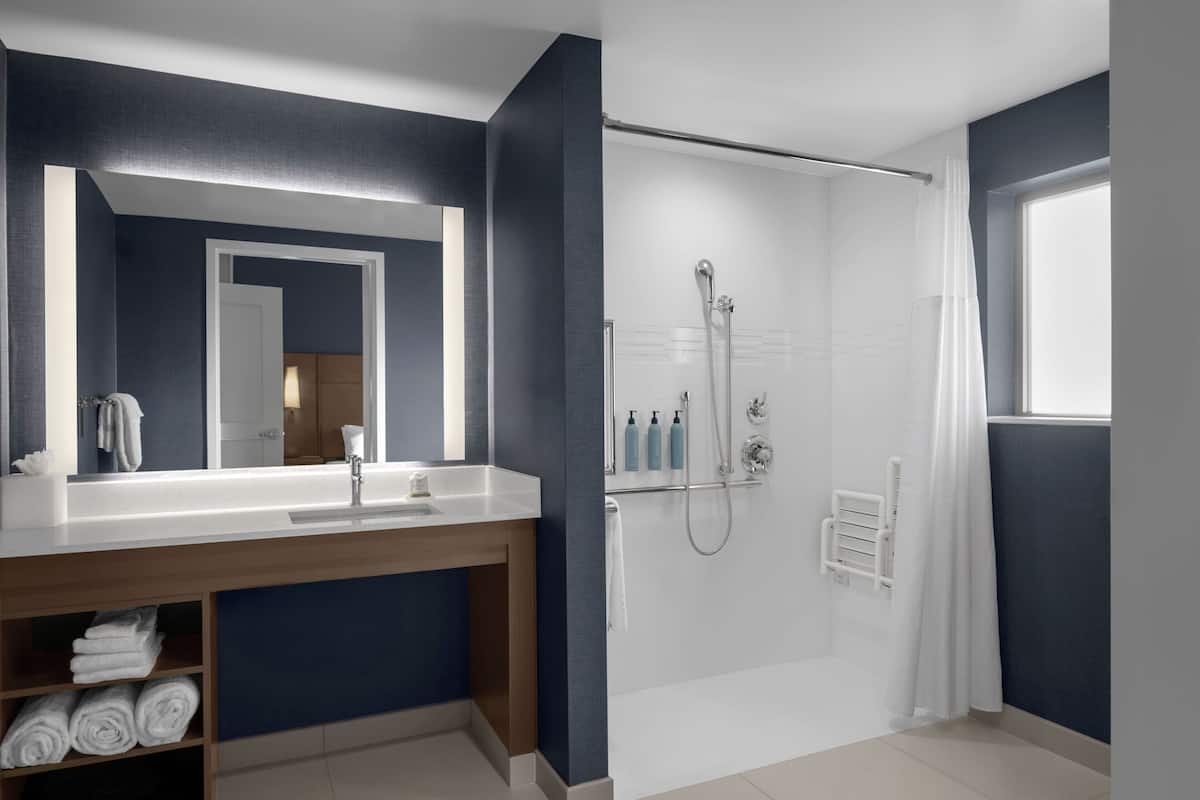 Un baño moderno con un espejo grande, lavamanos blanco y zona de ducha.