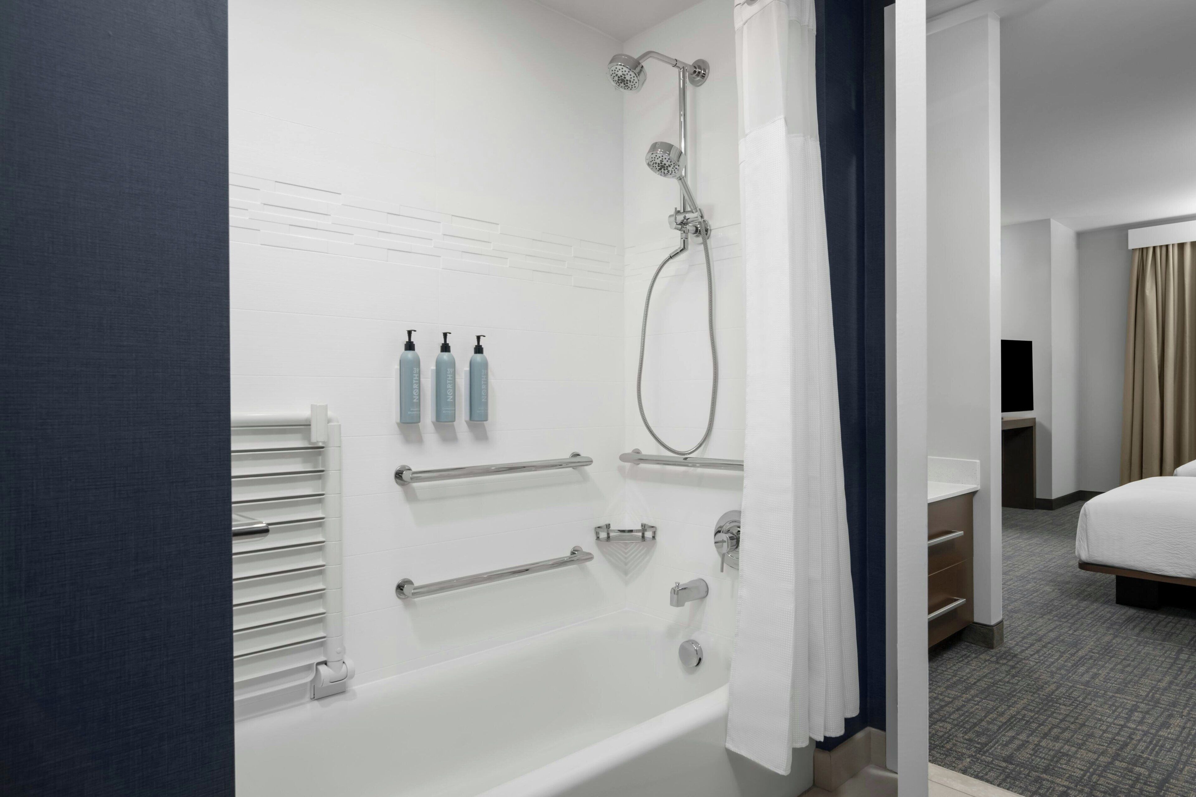 A modern bathroom with a bathtub, shower, and handrails.