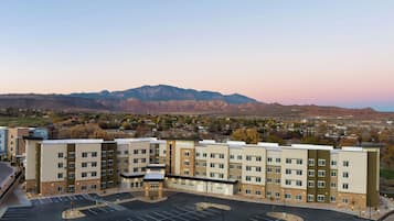 A multi-story hotel with a central courtyard, parking lot, and a mountain backdrop.