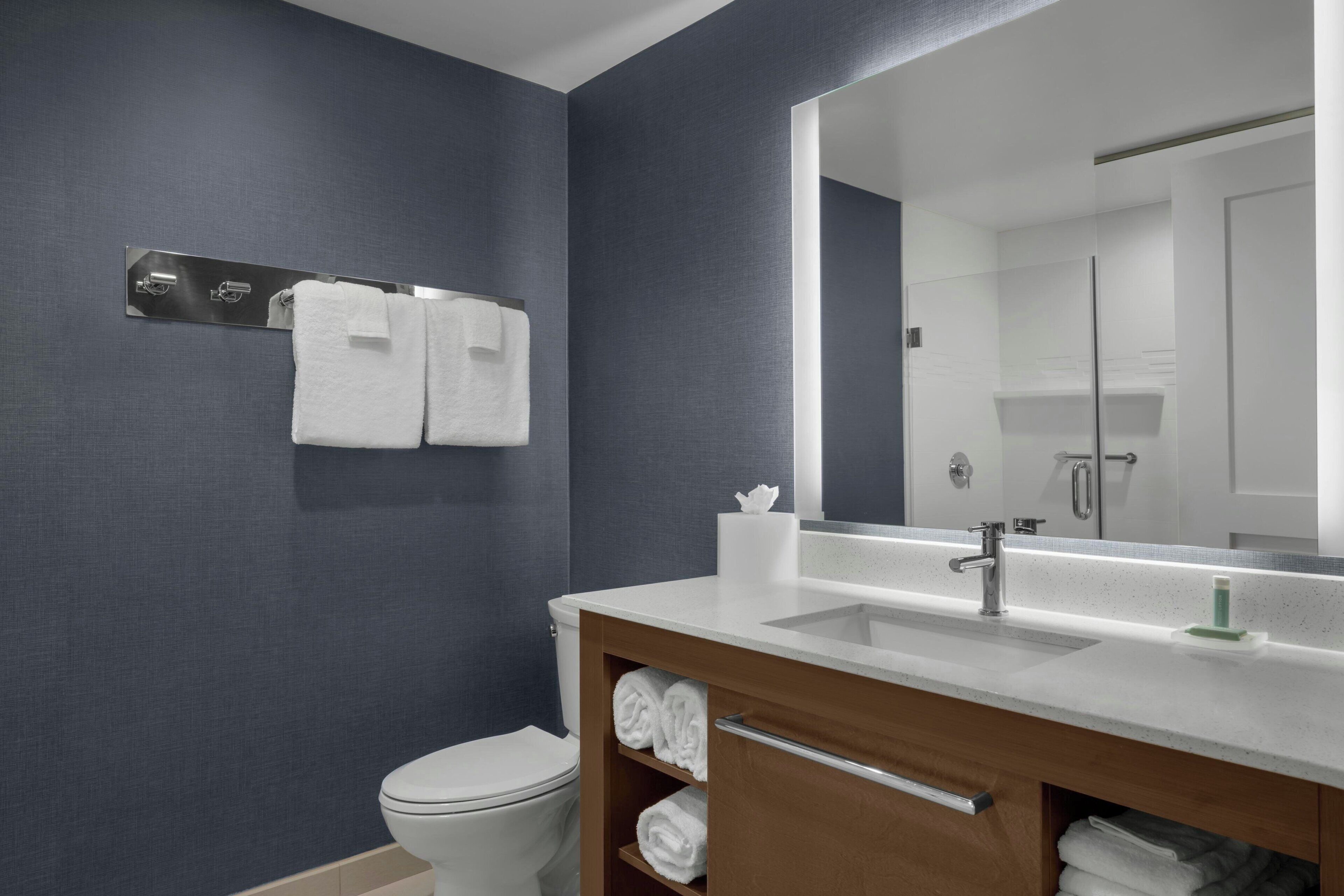 Un baño moderno con un lavamanos blanco, un espejo grande y un perchero para toallas.