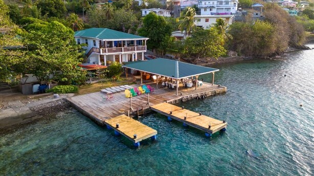 A waterfront property with a dock extending into clear water, a covered seating area, and a two-story building with balconies. - Hotel and restaurant in Bequia (Bequia)