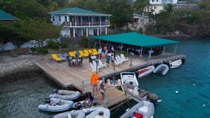 A dock with several boats, a covered seating area with yellow chairs, and a building with a green roof. - Hotel and restaurant in Bequia (Bequia)