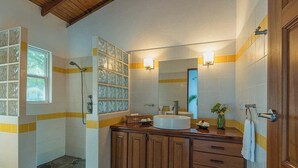 A bathroom with a glass shower enclosure, a wooden vanity with a sink, and a mirror above it. - Hotel and restaurant in Bequia (Bequia)