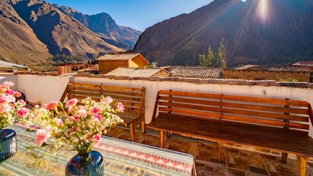 Una terraza con bancos de madera, una mesa con un florero y vista a la montaña.