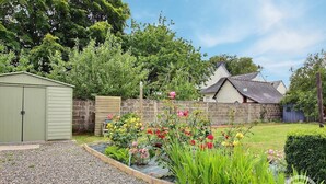 A garden with a shed, a stone wall, and a house with a sloped roof.