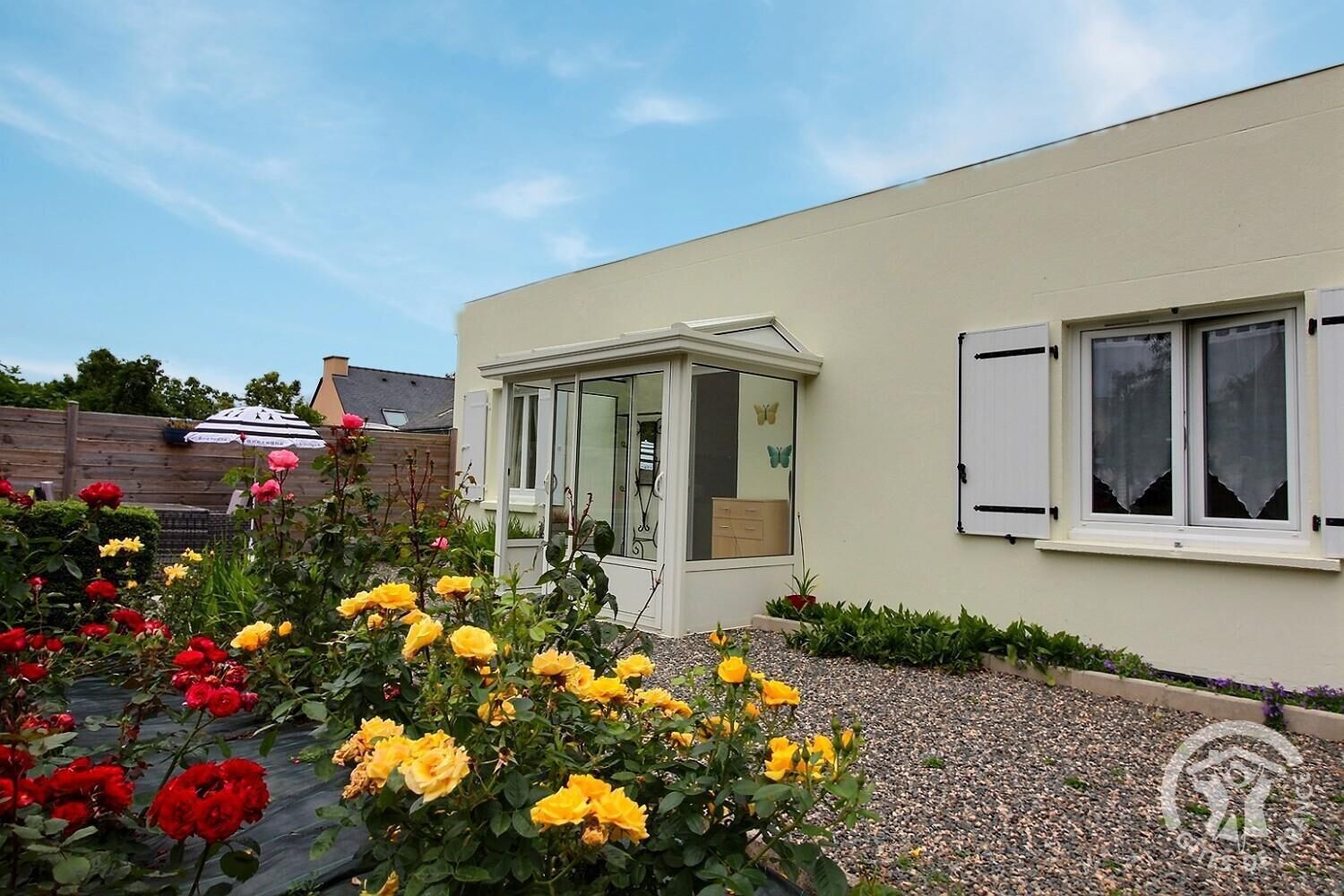 Ein Haus mit Wintergarten, ein Rosengarten und eine weiße Außenwand.