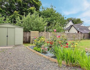 Un jardin avec un abri de jardin, un mur en pierre et une maison avec un toit en pente.