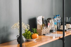A wooden shelf with a bowl of fruit, a vase with flowers, a coffee maker, and water bottles. - An Phu House Valley View (Dalat)