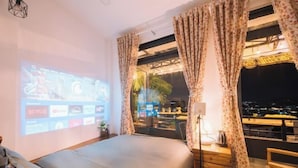 A bedroom with a bed, a desk, a lamp, and a projection screen displaying streaming services. - An Phu House Valley View (Dalat)