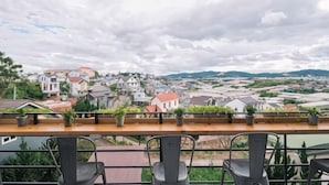 A terrace with a view of a town, a wooden table, and several chairs. - An Phu House Valley View (Dalat)
