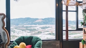 A room with a large window, a green chair with cushions, and a wooden table. - An Phu House Valley View (Dalat)