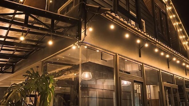 A building with a glass facade, outdoor seating area, and string lights. - An Phu House Valley View (Dalat)