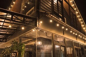 A building with a glass facade, outdoor seating area, and string lights. - An Phu House Valley View (Dalat)