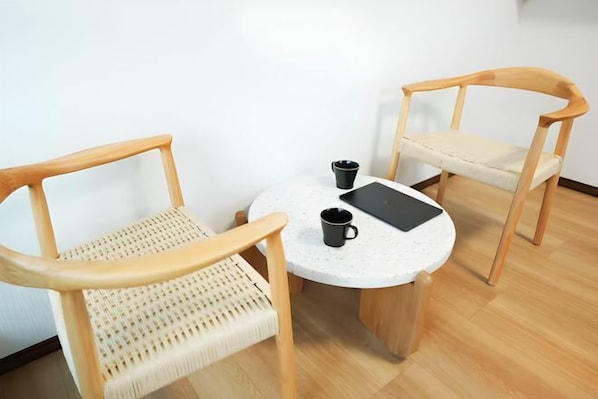 Una habitación con dos sillas de madera, una mesita redonda y una taza negra.