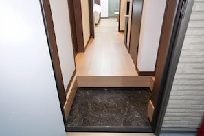 Un pasillo estrecho con suelo de madera, un escalón de mármol oscuro y una puerta blanca a la derecha.
