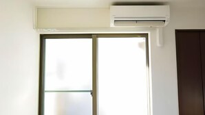 Een kamer met een schuifglazen deur, een airconditioning unit boven de deur bevestigd, en een donkerdeur rechts.