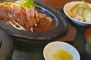A stone hot plate with sliced meat, a bowl of vegetables, and a small dish of sauce. - KAMI SUITES (Osaka)