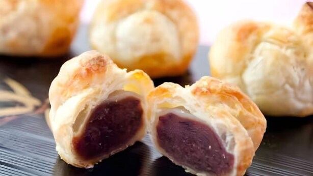 Un pastel con corteza dorada y relleno oscuro, posiblemente un tipo de bollo o masa rellena.
