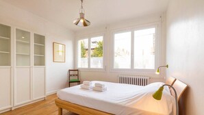 Ein Schlafzimmer mit Bett, Nachttischlampe, Fenster, Heizkörper und Einbauschrank.