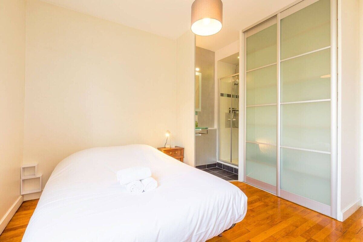 A bedroom with a bed, a nightstand, a sliding glass door leading to a shower area, and a wall-mounted light fixture.