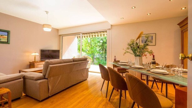 Ein modernes Wohnzimmer mit Sofa, Fernseher, Esstisch für sechs Personen und einem Balkon mit Aussicht.