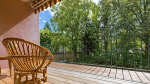 Eine Holzterrasse mit einem Korbstuhl, einem Metallgeländer und Bäumen im Hintergrund.