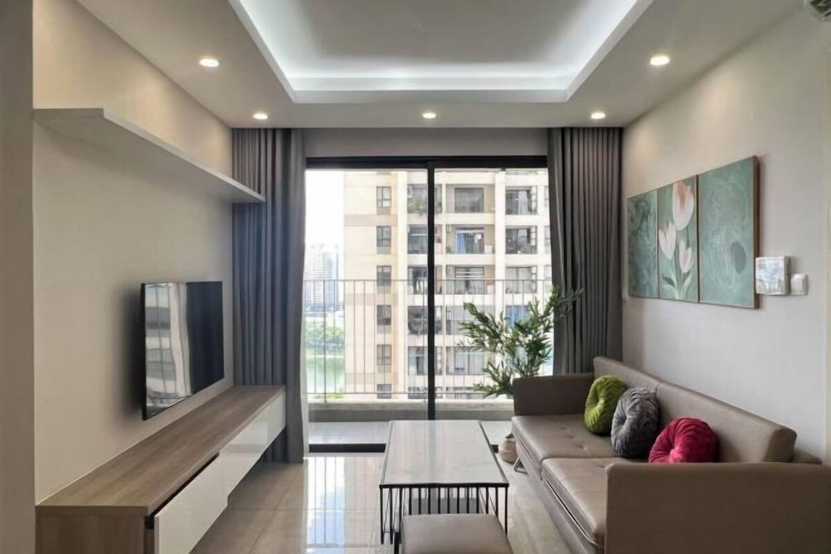 A modern living room with a flat-screen TV, a sofa, a coffee table, and a balcony with a city view.