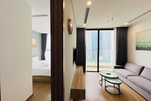 A modern hotel room with a bed, a sofa, a small table, and a large window with a view of buildings.