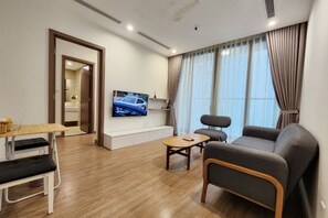 Een moderne woonkamer met een bank, een salontafel en een aan de muur bevestigde televisie. Er ligt een houten vloer en is een deur naar een andere kamer.