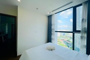 A bedroom with a large bed, a window with curtains, and a view of a cityscape. - Vinhomes Skylake - Kane Shining Star Apartment in Ha Noi (Hanoi)