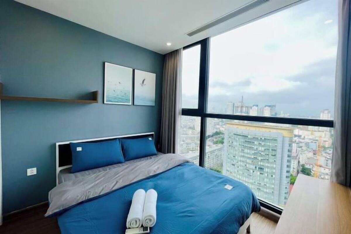 A modern hotel room with a large bed, a city view, and a window with curtains.