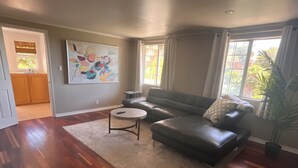 A living room with hardwood flooring, a leather sofa, a round coffee table, and a large abstract painting on the wall.