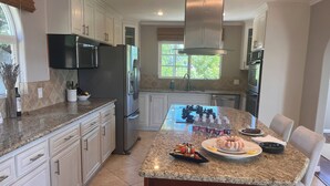 A modern kitchen with white cabinets, stainless steel appliances, a granite countertop, and a large island with food items.