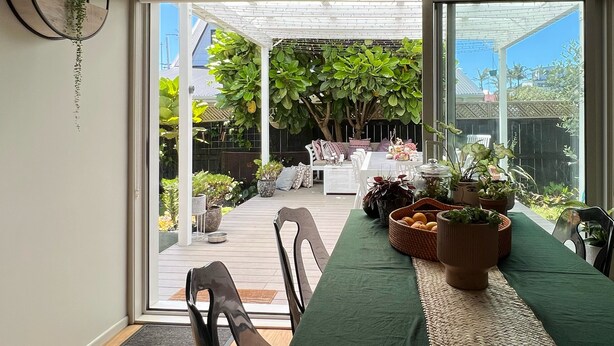 A dining area with a table set for four, surrounded by chairs, and a view of a garden with various plants and a seating area outside.