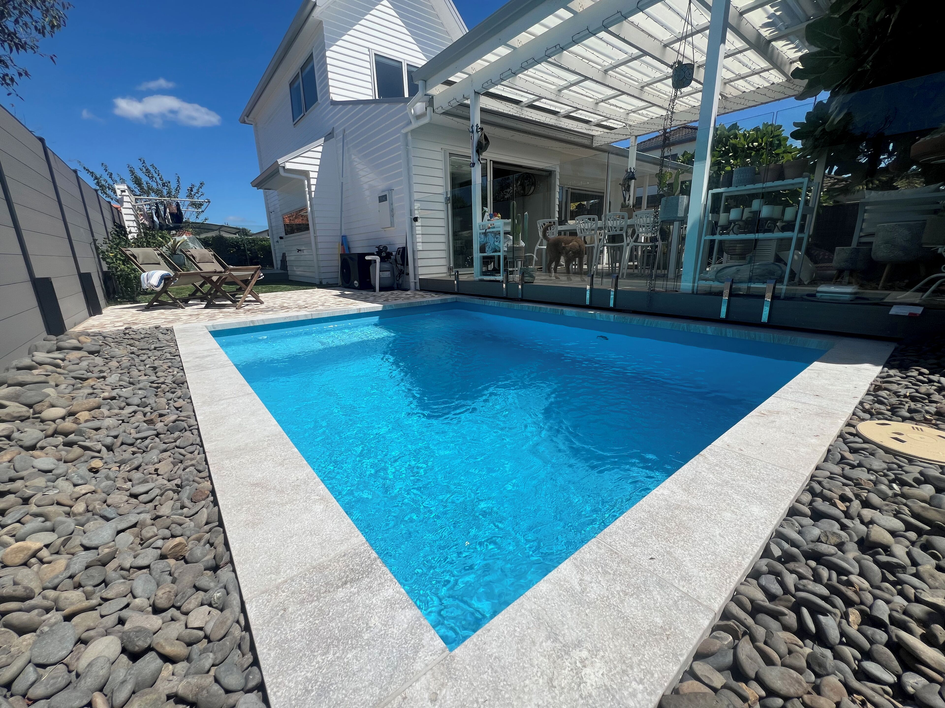 Una piscina rettangolare con bordo in pietra, circondata da un patio con sedie e tavolo.