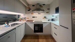 A compact kitchen with white cabinets, a wooden countertop, a built-in dishwasher, and a tiled backsplash with multicolored tiles.