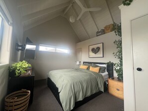 A bedroom with a bed, bedside table, dresser, and a window. - Papamoa beach house with pool and indoor outdoor living (Tauranga)